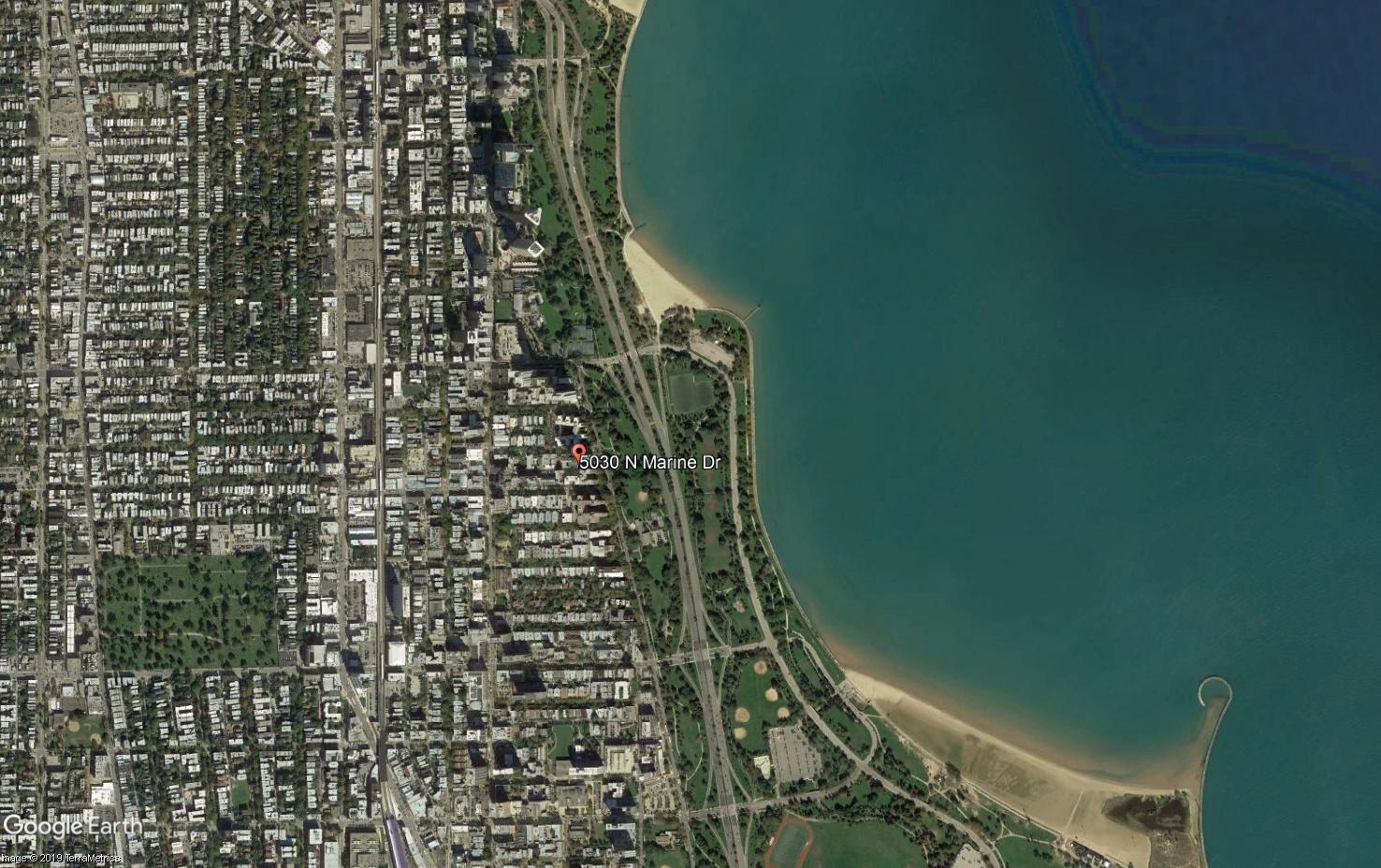 Aerial view of rows upon rows of buildings on the left, with a green buffer and the shores of Lake Michigan on the right.