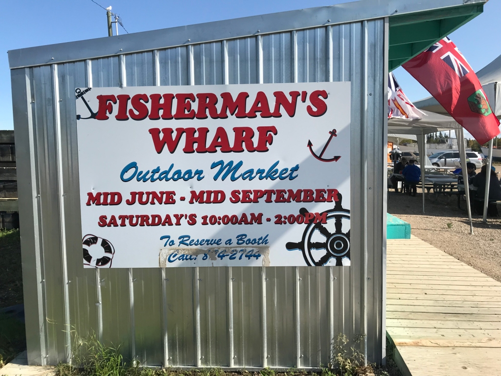 A sign on the side of a metal shed advertises the Saturday Market at Fisherman's Wharf. 