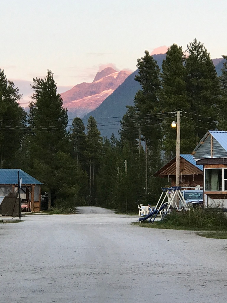 A driveway runs between cabin buildings, with a forest behind and a mountain towering over the scene. 